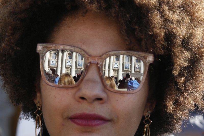 The banners of new saints are reflected in a woman's sunglasses before the canonization Mass for five new saints celebrated by Pope Francis in St. Peter's Square at the Vatican Oct. 13, 2019. (CNS photo/Paul Haring)
