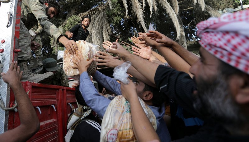 Turkey-backed Syrian rebel fighters hand bread to civilians in the border city of Tal Abyad, Syria, Oct.15, 2019. Humanitarian concerns are growing as people caught in the crosshairs of the Turkish incursion into northeastern Syria try to flee for safety, and groups are scrambling to aid them. (CNS photo/Khalil Ashawi, Reuters)