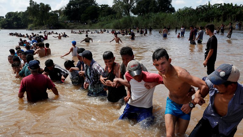 Migrants, part of a caravan traveling to the United States, form a human chain Oct. 29, 2019, to cross the river from Guatemala to Mexico. The Guatemalan bishops' migrant ministry has rejected talk of the U.S. and Guatemalan governments sending asylum seekers from third countries to a remote and rugged jungle region rife with drug cartel activities, saying conditions are not secure for citizens, much less migrants. (CNS photo/Leah Mills, Reuters)