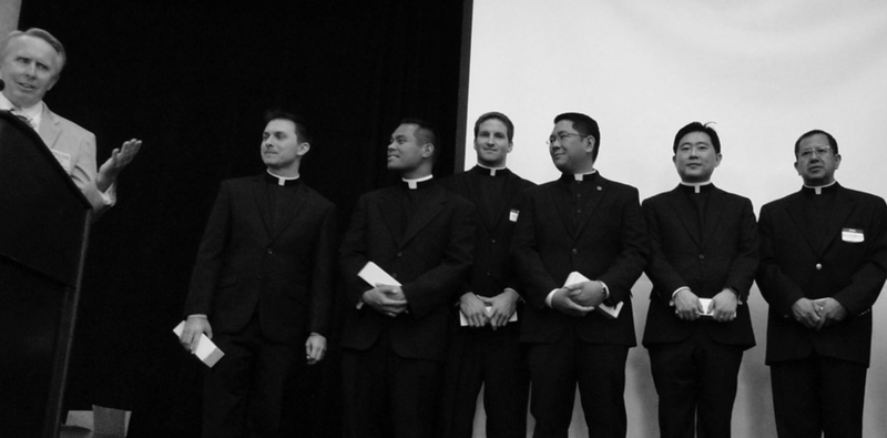 Ed Lupton at the podium in front of six newly ordained priests at the 2015 Ordinati Luncheon. (Courtesy © Bill Garcia Solis)