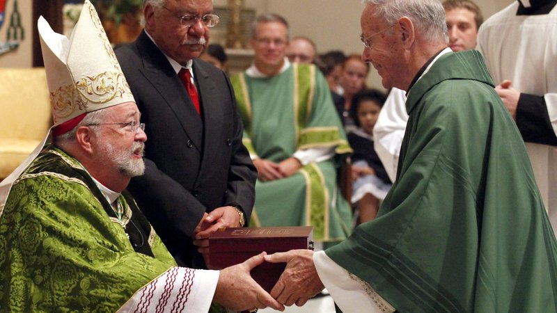 Bishop Daniel R. Jenky of Peoria, Ill., hands a copy of the "positio" on Archbishop Fulton J. Sheen's life to Father James O'Brien, representing the late Cardinal Francis E. George and the Archdiocese of Chicago, during a Mass at the Cathedral of St. Mary of the Immaculate Conception in Peoria Sept. 9, 2012. Supporters of the canonization cause for Archbishop Sheen are invited to participate in a nine-day novena starting Dec. 12, 2019, to "petition God unceasingly to remove all obstacles" for the beatification of the media pioneer, author and evangelist. Archbishop Sheen's beatification was scheduled for Dec. 21 but has been postponed. (CNS photo/Karen Callaway, Catholic New World)