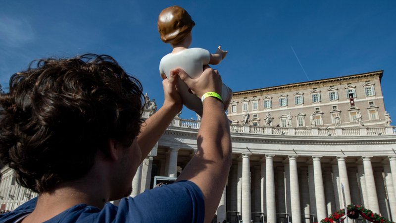A pilgrim holds up a figurine of the Christ Child as Pope Francis leads the Angelus from the window of his studio overlooking St. Peter's Square at the Vatican Dec 15, 2019. (CNS photo/Vatican Media)