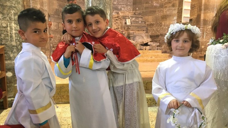 Easter Sunday, Batnaya, Northern Iraq, 2017. Chaldean Catholics celebrate the first Easter Sunday in their church in more than two years. In 2014, ISIS had overrun the Christian town and displaced all of its people for more than two years. Note the destroyed and bullet-scarred former altar in the background. In October 2017, the town would be occupied a second time, now by Iranian-backed paramilitary units, which remain in control of the surrounding territory today. (Photo permission of Stephen M. Rasche)