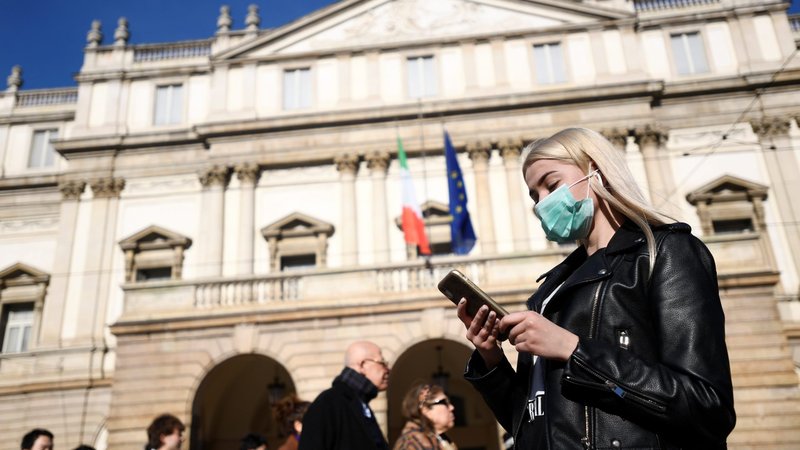 A woman wearing a face mask checks her phone outside the Teatro alla Scala opera house, closed by authorities due to a coronavirus outbreak in Milan Feb. 24, 2020. The Archdiocese of Milan issued a notice Feb. 23 suspending all public celebrations of Mass until further notice in compliance with Italian Ministry of Health precautions to prevent the further spread of the coronavirus. (CNS photo/Flavio Lo Scalzo, Reuters)