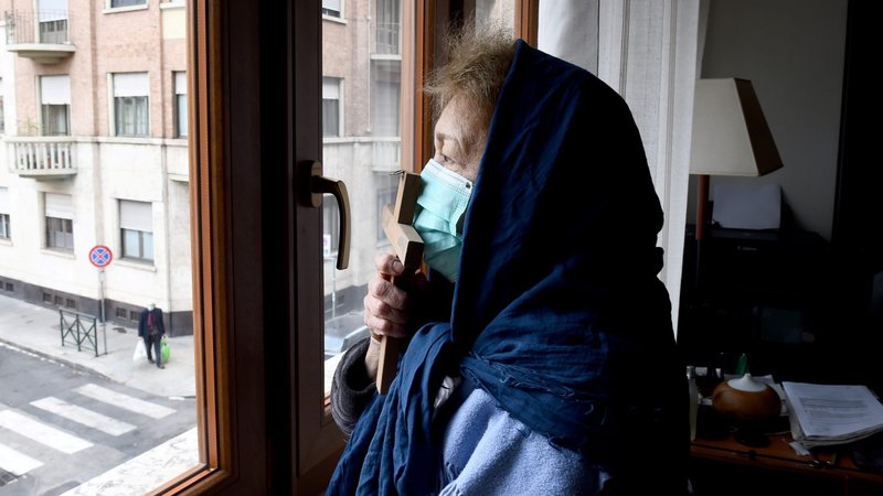 A woman wearing a protective face mask kisses a cross as she prays from the window of her home in Turin, Italy, March 25, 2020. (CNS photo/Massimo Pinca, Reuters)