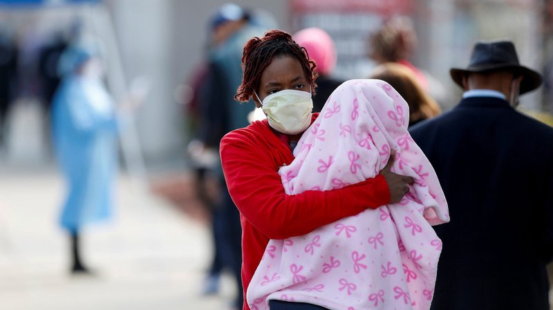 A woman in Chicago holds a child as she walks past people waiting in line to receive the coronavirus test April 7, 2020. (CNS photo/Joshua Lott, Reuters)