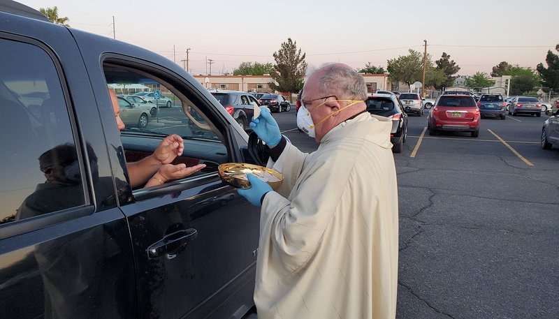 Bishop Peter Baldacchino of Las Cruces, N.M., wears a mask and gloves while giving Communion to a passenger of a vehicle during the Easter Vigil in the parking lot of the Cathedral of the Immaculate Heart of Mary in Las Cruces April 11, 2020. Bishop Baldacchino became the first-known U.S. prelate to lift a diocesan ban on public Mass April 15, 2020, and told priests they may resume sacramental ministry if they follow state health mandates. (CNS photo/courtesy David McNamara, Diocese of Las Cruces)