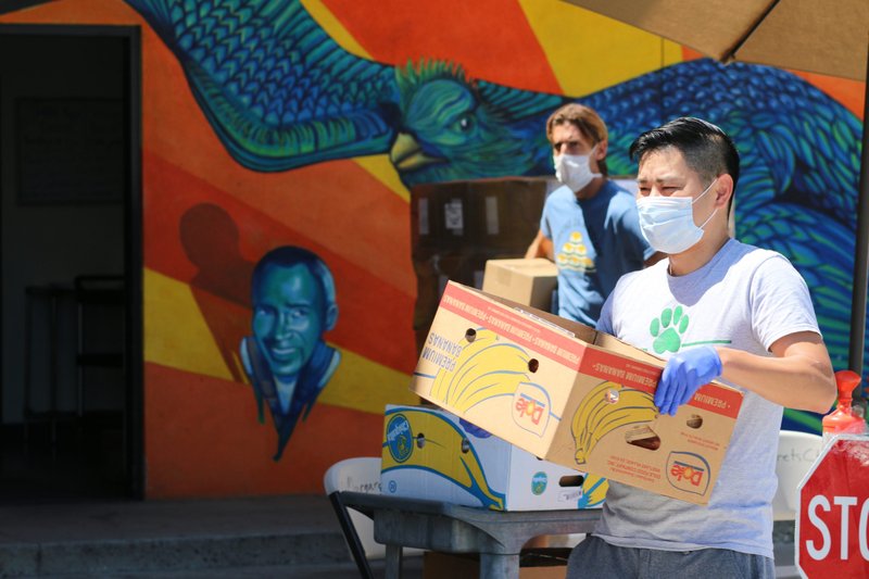 A Catholic Charities worker and a volunteer carry boxes to food to people's cars in the driveway of St. Margaret's Center. (Pablo Kay)
