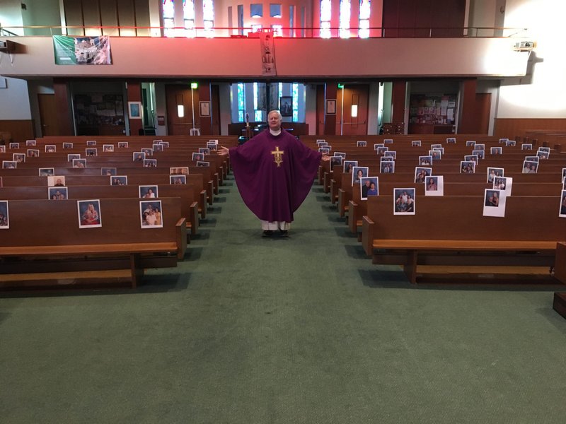 Msgr. Richard Martini, pastor of St. Joseph Church in Carpinteria, poses with pictures of his parishioners taped to pews in the church in late March. First done by a pastor in Italy during the onset of the coronavirus (COVID-19) pandemic, the gesture is meant to show solidarity with parish communities at a time when many churches are shuttered to help “flatten the curve” of the coronavirus outbreak, but priests continue to celebrate private, often livestreamed Masses. (St. Joseph Church, Carpinteria)
