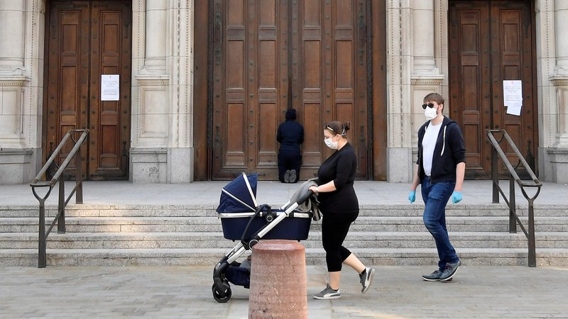 People wearing protective masks walk as a person prays at the closed doors of London's Westminster Cathedral on Easter, April 12, 2020, during the COVID-19 pandemic. Churches in England and Wales must wait until July before they may reopen under a coronavirus recovery strategy published by the government. (CNS photo/Toby Melville, Reuters)