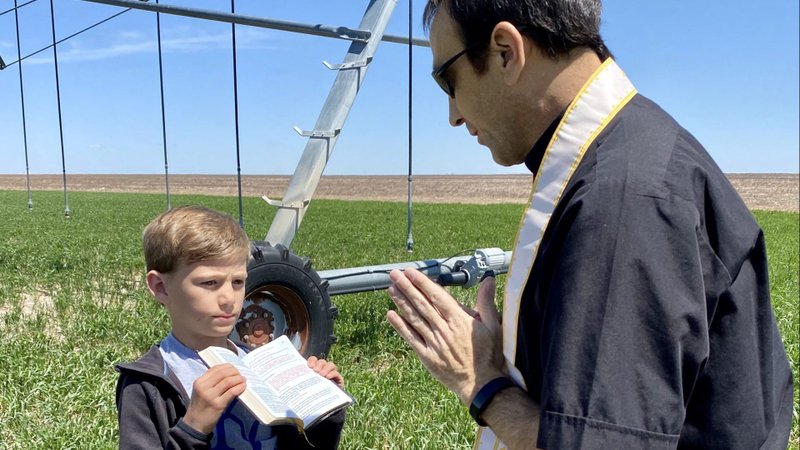 Brett Koster holds a prayer book as Father Michael Leiker blesses a field on the Koster's farm near Colby, Kan., May 6, 2020. Catholics are being asked to remember priests as their "spiritual fathers" on Father's Day June 21, 2020. (CNS photo/courtesy Karen Bonar, The Register)