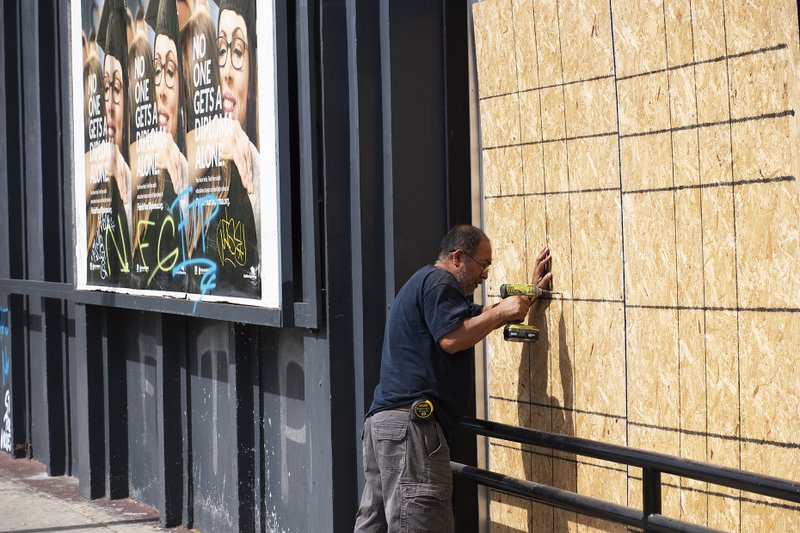 A man covers the windows of a business on Melrose Avenue in Los Angeles with plywood May 31 after a night of rioting and looting. (Victor Alemán)