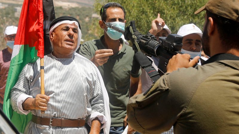 A demonstrator holds a Palestinian flag in front of Israeli forces during a protest against Israel's plan to annex parts of the occupied West Bank, near Nablus July 3, 2020. (CNS photo/Raneen Sawafta, Reuters)