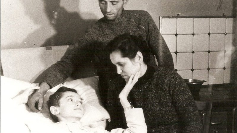 Angiolino Bonetta lying in bed, with his parents beside him. (Image via Facebook @servodidioangiolinobonetta)