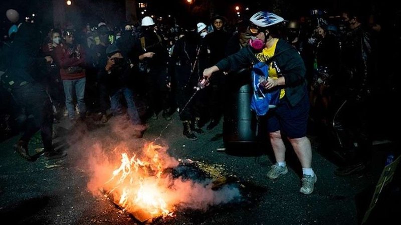 A demonstrator tries to put out a fire that other demonstrators started outside a U.S. courthouse during a protest on July 31, 2020 in Portland, Oregon. (Alisha JUCEVIC / AFP via Getty via CNA)