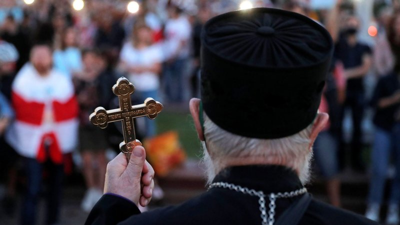 A clergyman holds a cross as he stands in front of participants during an opposition demonstration at Independence Square in Minsk, Belarus, Aug. 24, 2020. The crowds were protesting the results of the Aug. 9 presidential election. (CNS photo/Vasily Fedosenko, Reuters)