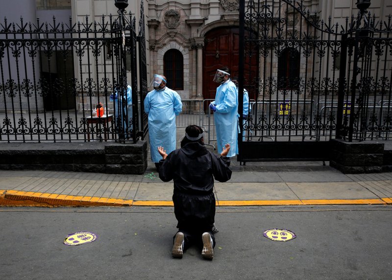 A woman kneels in prayer in front of guards wearing personal protective equipment outside the Monastery of the Nazarenes in Lima, Peru, Oct. 7, 2020, as churches continue to be closed during the COVID-19 pandemic. (CNS photo/Sebastian Castaneda, Reuters)
