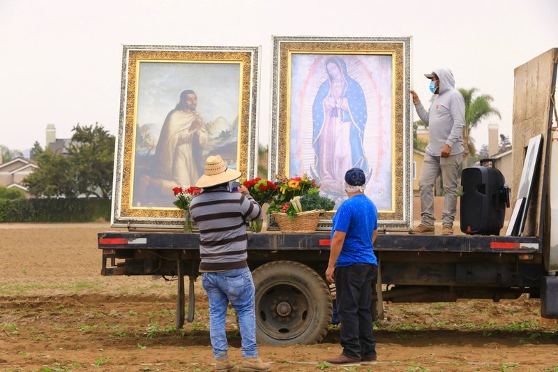 Trabajadores agrícolas colocan flores y verduras frente a las imágenes peregrinas de Nuestra Señora de Guadalupe y San Juan Diego en la primera parada de la peregrinación por las parroquias de la Arquidiócesis de Los Ángeles el 22 de octubre. (David Amador Rivera / Angelus News)