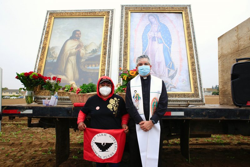 Father Ochoa poses with a farmworker in front of the images. (David Amador Rivera/Angelus News)