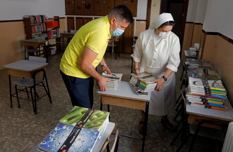 Teachers place disinfected books on desks as they prepare a classroom at Immaculate and St. Joseph of the Mountain School in Ronda, Spain, Aug. 28, 2020, before students return in September during the COVID-19 pandemic. Catholics in Spain are angry about a new education law that would downgrade religious teaching and restrict state funding for Catholic schools. (CNS photo/Jon Nazca, Reuters)