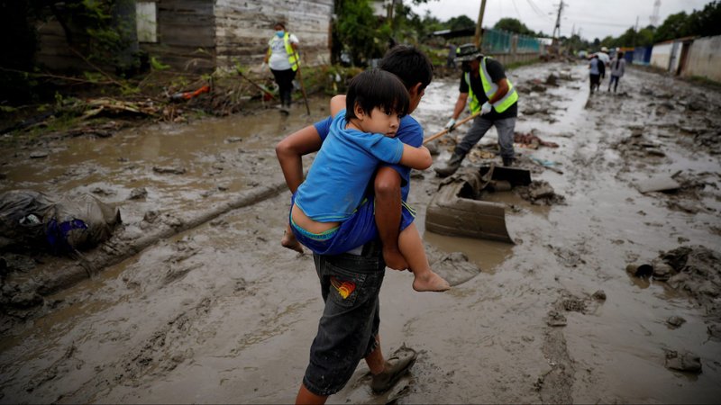 A child in La Lima, Honduras, carries his brother in a street covered in mud Dec. 8, 2020, after flood waters caused by Hurricanes Eta and Iota receded. (CNS photo/Jose Cabezas, Reuters)