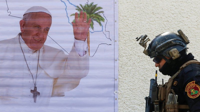 A security agent walks near posters of Pope Francis in Baghdad March 3, 2021. When the pope visits Iraq March 5-8, he will undertake a risky trip to a war-torn country that has seen recent rockets attacks and is surging with new COVID-19 cases. (CNS photo/Khalid al-Mousily, Reuters)