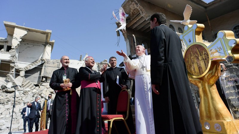 Pope Francis releases a white dove near during a memorial prayer for the victims of the war at Hosh al-Bieaa (church square) in Mosul, Iraq, March 7, 2021. The large gold cross at right was made by Iraqi architect Omar Carona. A sculpture of a white dove sits on top of the cross; two hands, representing Mosul's men and women, hold the Christian symbol. (CNS photo/Vatican Media)