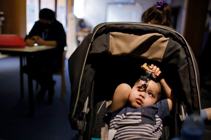A baby sits in his stroller at La Colaborativa in Chelsea, Mass., March 23, 2021, while his mother fills out paperwork for help with her rent payment. (CNS photo/Brian Snyder, Reuters)