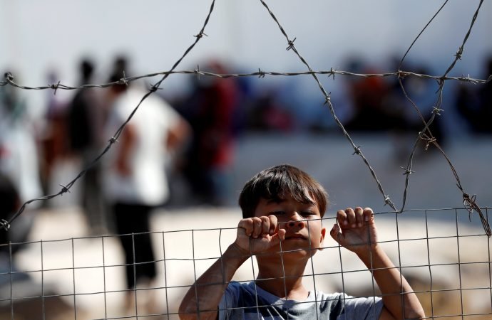 A displaced child from the Moria refugee camp looks over a fence inside a new temporary camp on the Greek island of Lesbos Sept. 23, 2020. The Moria camp, which was mostly destroyed in fires Sept. 9, was home to at least 12,000 people, six times its maximum capacity of just over 2,000 asylum-seekers. (Yara Nardi/Reuters via CNS)
