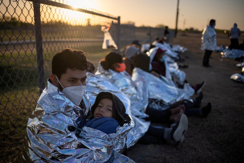 An asylum-seeker from Honduras holds his 6-year-old son in La Joya, Texas, March 19, 2021, as they awake near a baseball field after crossing the Rio Grande. Emergency blankets were provided to the group of about 150 migrants from Central America by Border Patrol agents. (CNS photo/Adrees Latif, Reuters)