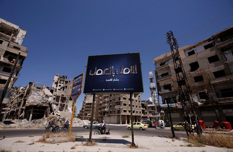 A billboard that reads "Hope through work. Bashar al-Assad" is seen near damaged buildings in Homs, Syria, May 23, 2021, ahead of the May 26 presidential election. (Omar Sanadiki/Reuters via CNS)