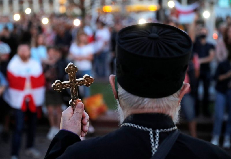 A clergyman holds a cross as he stands in front of participants during an opposition demonstration at Independence Square in Minsk, Belarus, Aug. 24, 2020. The crowds were protesting the results of the Aug. 9 presidential election. (CNS photo/Vasily Fedosenko, Reuters)