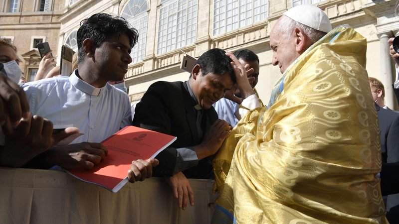 Pope Francis, accepting the gift of a shawl, blesses a priest during his general audience in the San Damaso Courtyard of the Apostolic Palace at the Vatican June 30, 2021. The pope continued his series of audience talks focused on the Letter to the Galatians and reflected on St. Paul's life and the power of God's grace. (CNS photo/Vatican Media)