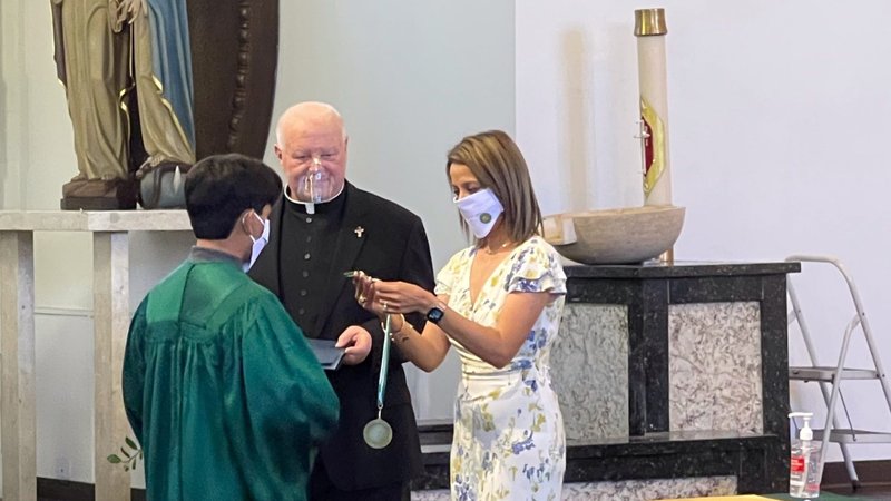 St. Raymond principal Claudia Rodarte and parish pastor Fr. John Higgins present the school's Academic Excellence medal to a graduating 8th grader in June 2021. (Courtesy photo)