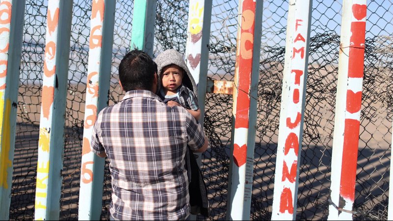 A man in Tijuana, Mexico, holds his son next to a section of the wall separating Mexico and the United States. (CNS photo/Mohammed Salem, Reuters)