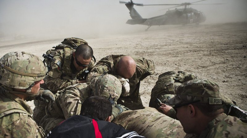 A translator and soldiers from 1st Platoon Alpha Company, 1st Battalion, 36th Infantry Regiment take cover from a helicopter's rotor wash in Demaiwand, Afghanistan, Jan. 18, 2013, while evacuating a 10-year-old girl injured by an improvised explosive device that detonated about 875 yards away. (CNS photo/Andrew Burton, Reuters)