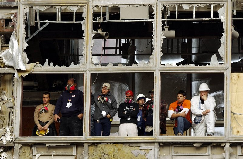 One month after the terrorist attack on the World Trade Center, workers pause to watch a memorial service from a damaged pedestrian bridge overlooking the site of the fallen buildings in New York Oct. 11, 2001. A short service at ground zero marked the tragic event. (CNS photo from Reuters)