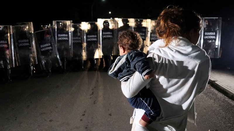 A migrant woman in Huixtla, Mexico, carries her baby Sept. 5, 2021, as members of the National Guard block the street during an operation to dissolve a caravan of migrants and asylum seekers from Central America and the Caribbean. (CNS photo/Jose Torres, Reuters)