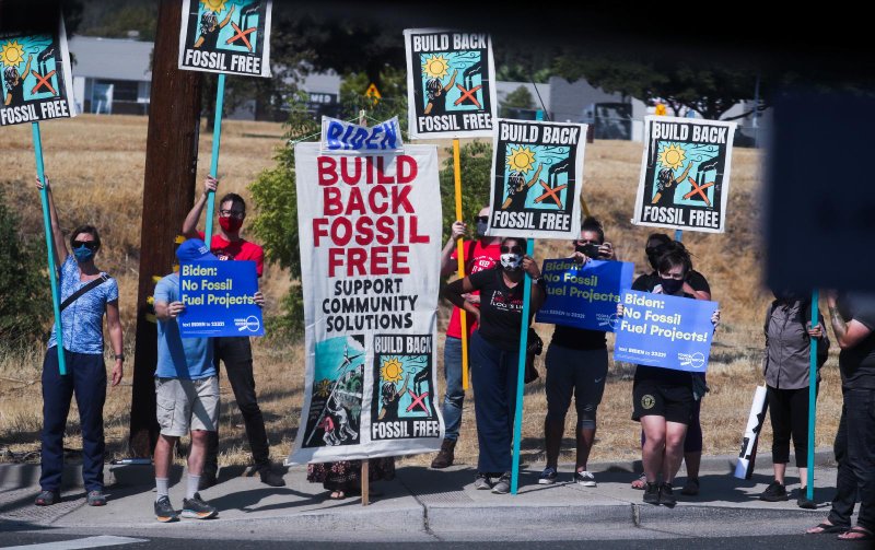 Environmental activists in Mather, Calif., hold signs along a road Sept. 13, 2021, as the car carrying President Joe Biden drives by. (CNS photo/Leah Millis, Reuters)
