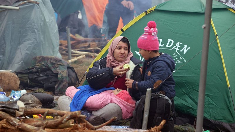 A woman and child share an apple outside a tent near barbed wire fence as migrants attempt to cross the border with Poland from Belarus Nov. 10, 2021. Hundreds of migrants shivered in freezing temperatures and huddled round campfires on the Belarusian border with Poland; aid agencies have accused Poland of blocking proper asylum procedures and contributing to refugee deaths from hypothermia and exhaustion. (CNS photo/Leonid Scheglov, BelTA handout via Reuters)