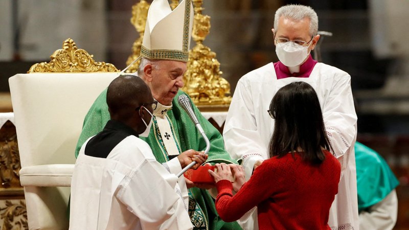 A new lector receives a Bible from Pope Francis during a Mass marking Sunday of the Word of God in St. Peter's Basilica at the Vatican Jan. 23, 2022. At the Mass, the pope formally installed women and men in the ministries of lector and catechist. (CNS photo/Remo Casilli, Reuters)