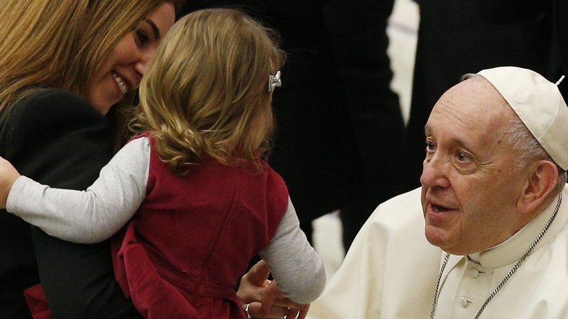 Pope Francis greets a woman and child during his general audience in the Paul VI hall at the Vatican Jan. 26, 2022. The pope explained to the crowd that he had a problem with inflammation in his right knee and that he wouldn't be able to go greet them as usual. Instead the crowd came to him. (CNS photo/Paul Haring)