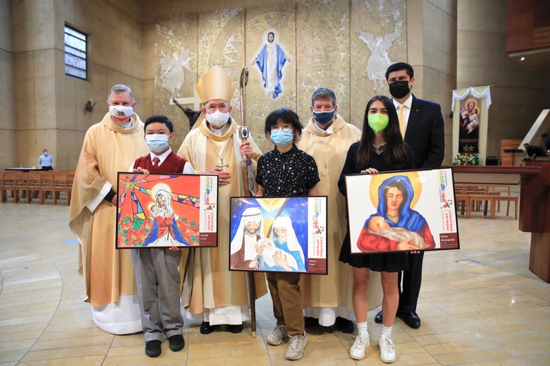 From left: Jacob Cruz, Justina Yoon, and Mina Michalski pose with their award-winning artwork at the Missionary Childhood Association Mass Oct. 20, 2021, at the Cathedral of Our Lady of the Angels. Behind them, from left to right are: Msgr. Kieran E. Harrington, national director of the Pontifical Mission Societies in the U.S.; Archbishop José H. Gomez, and Msgr. Terrance Fleming, Pontifical Mission Societies executive director for the Archdiocese of Los Angeles, and Catholic Schools superintendent Paul Escala. (David Amador Rivera)