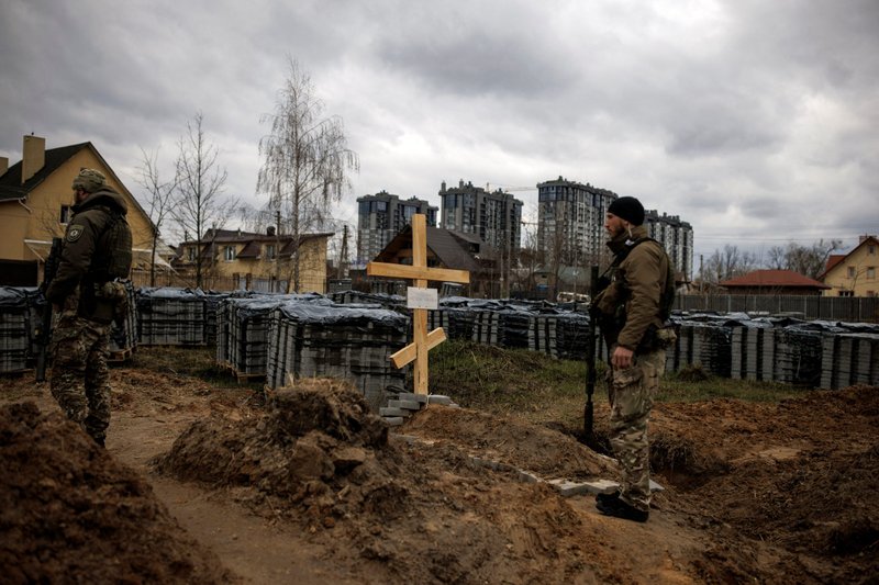Ukrainian soldiers stand next to the grave of a civilian in Bucha, Ukraine, April 6. (CNS/Alkis Konstantinidis, Reuters)