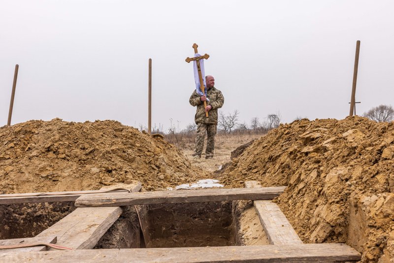 A Ukrainian soldier holds a crucifix by the grave where his comrade is to be laid to rest in Starychi, Ukraine, March 16, 2022, during the Russian war. (CNS photo/Alex Kent)