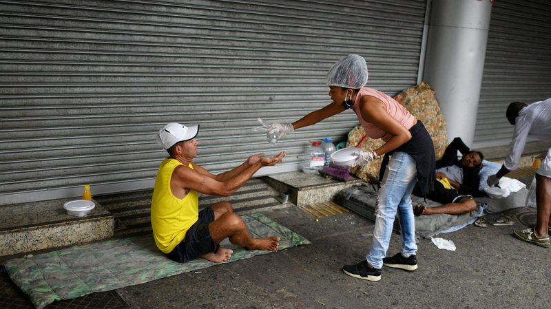 A woman from Rio de Janeiro disinfects the hands of a homeless man as she delivers him a meal April 11, 2020. The senselessness of war produces tremendous poverty, and its violence strikes those who are defenseless and vulnerable, Pope Francis said in message for the World Day of the Poor, which will be marked Nov. 13, 2022. (CNS photo/Lucas Landau, Reuters)