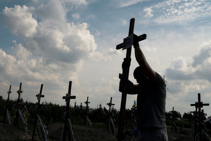 A volunteer places a cross with a number on a grave of an unidentified person during a mass burial ceremony in Bucha, Ukraine, Aug. 17, 2022, as Russia's attack on Ukraine continues. (CNS photo/Valentyn Ogirenko, Reuters)