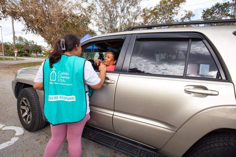 A volunteer for Catholic Charities of the Diocese of Venice, Fla., greets a survivor of Hurricane Ian Oct. 5, 2022, at a Catholic Charities site in Bonita Springs, where staff and volunteers operate a drive-up emergency food and water distribution. (CNS photo/Tom Tracy)