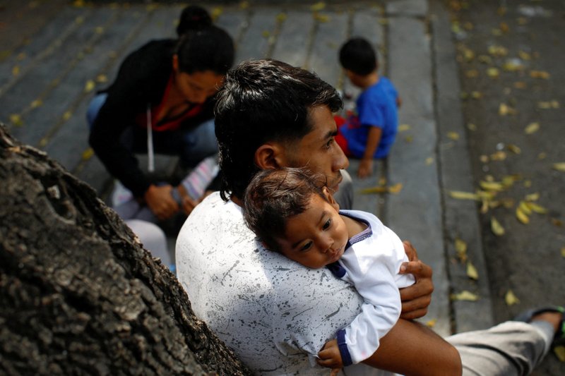 A Venezuelan migrant in Mexico City holds his baby Oct. 27, 2022, as he waits on the sidewalk with his family outside the Mexican Commission for Aid to Refugees. (CNS photo/Raquel Cunha, Reuters)