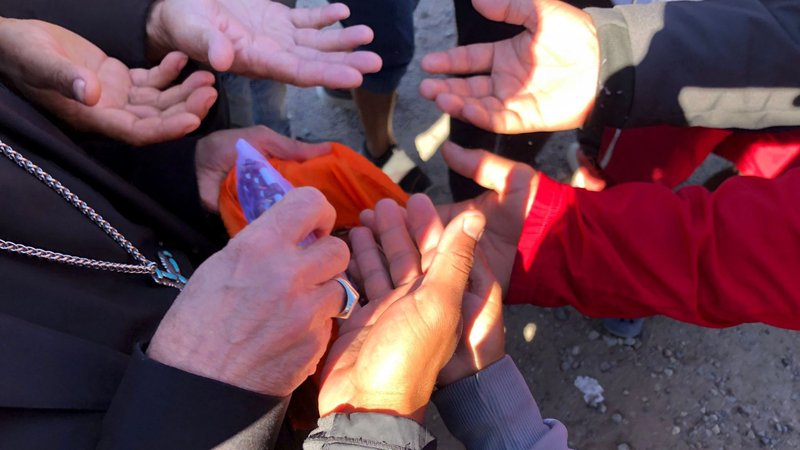 Venezuelan migrants squeeze in to grab a rosary from the hands of Bishop Mark J. Seitz of El Paso, Texas, during his visit to a tent camp on the banks of the Rio Grande on the Mexico side close to El Paso Oct. 29, 2022. The bishop has spoken out against the measure known as Title 42, which keeps certain migrants out of the U.S. citing health measures deemed necessary during the coronavirus pandemic. (CNS photo/courtesy Hope Border Institute)